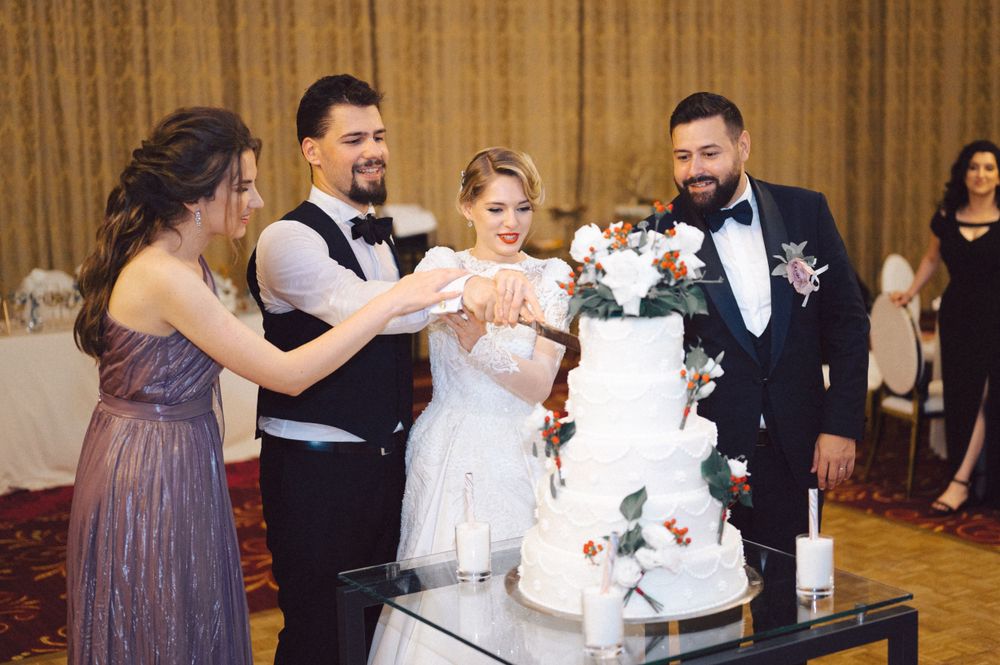 Wedding party gathered around elegant white tiered cake with floral decorations.