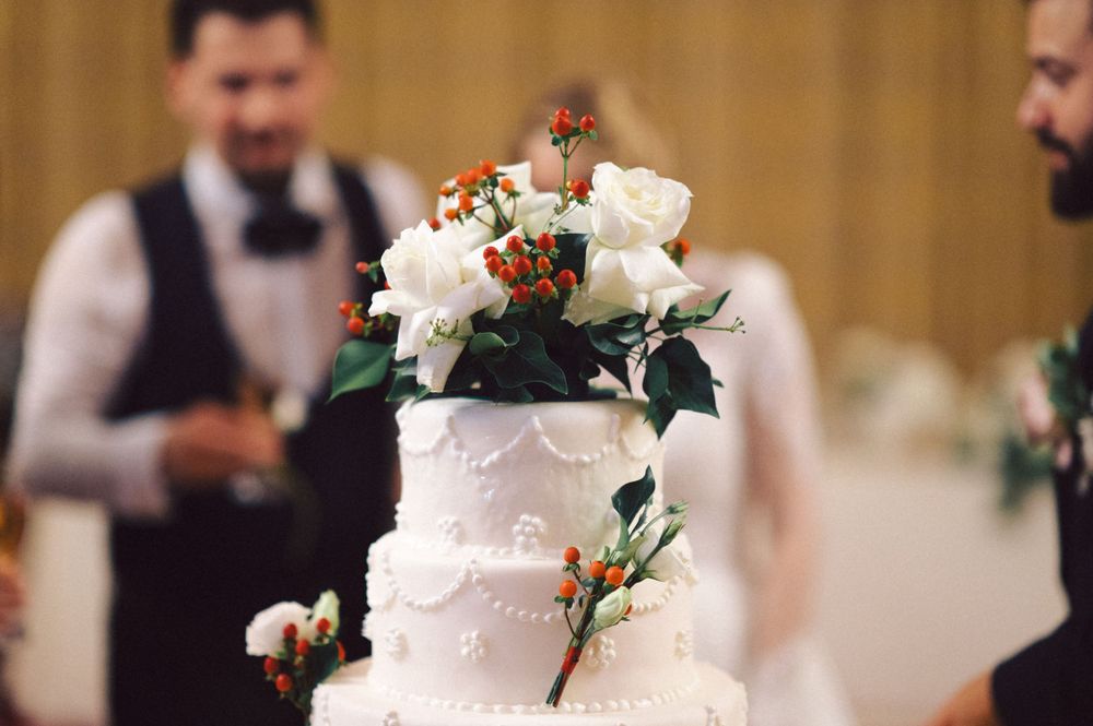 Elegant white wedding cake decorated with fresh flowers and greenery on display at a reception.