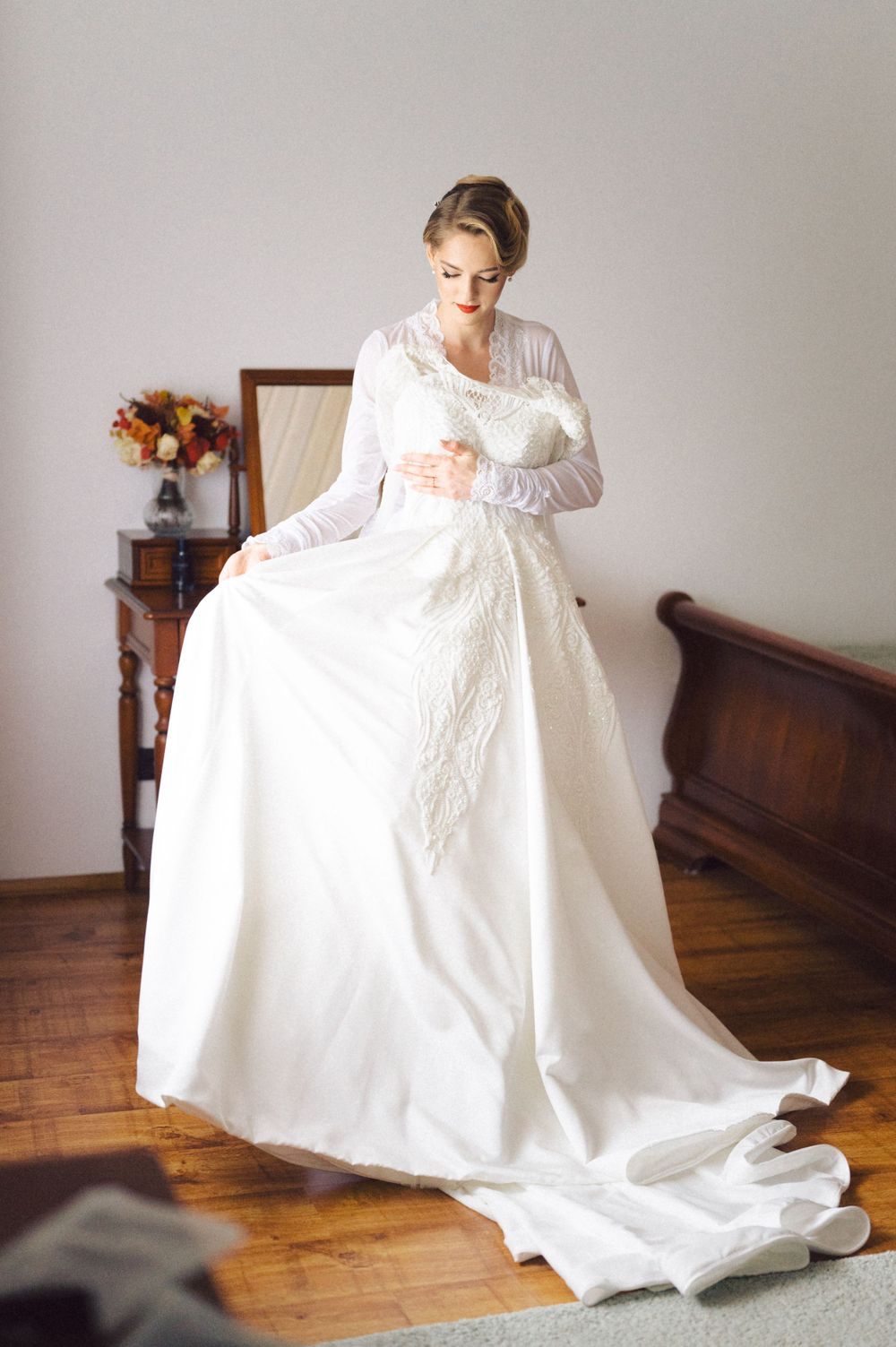 Elegant wedding dress being prepared in a room with hardwood floors and antique furniture.