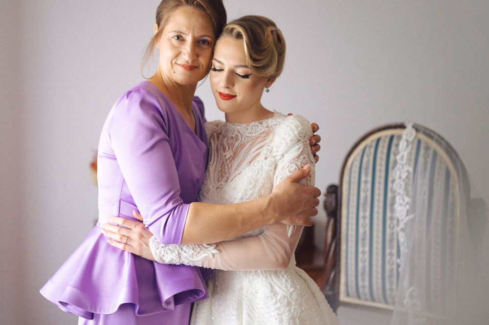 Tender moment shared between two wedding attendants in purple and white dresses.