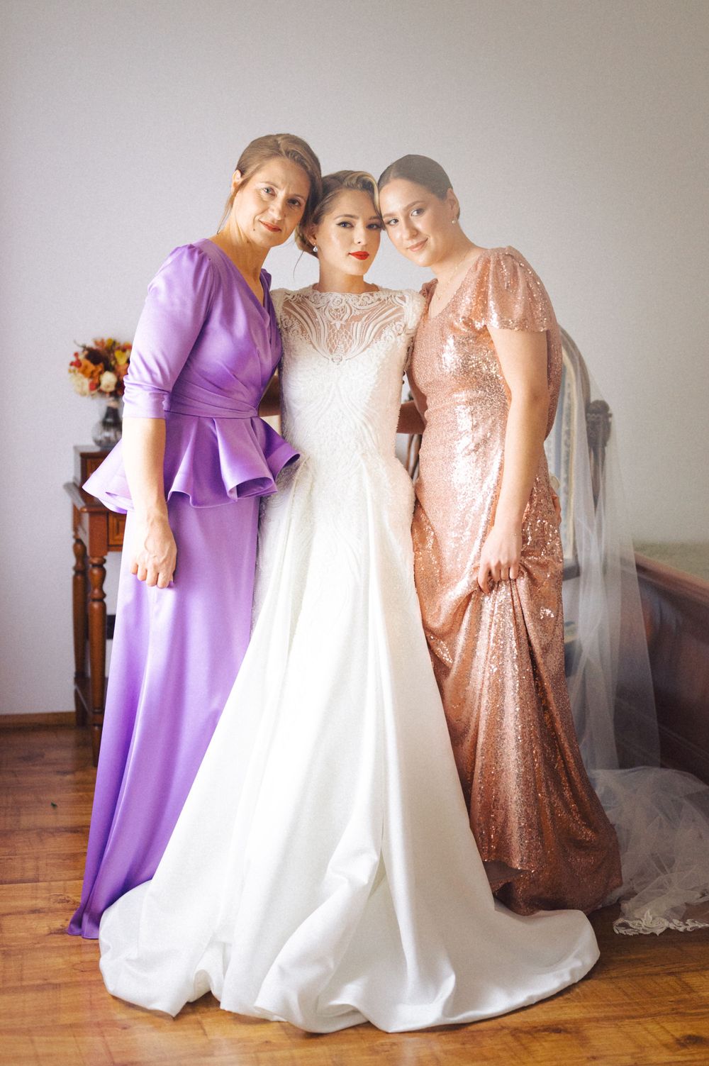 Three attendants pose in coordinating formal dresses in purple, white, and rose gold.