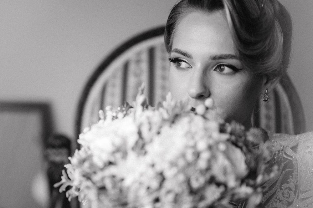 Close-up black and white portrait of bride holding floral bouquet near her face.