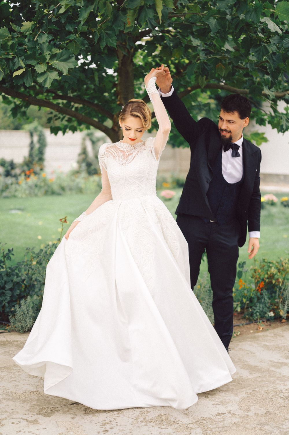 A couple dancing in formal wedding attire under green trees in a garden.
