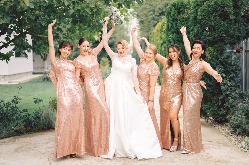 Bridesmaids in sparkling rose gold dresses celebrating with bride in white gown.