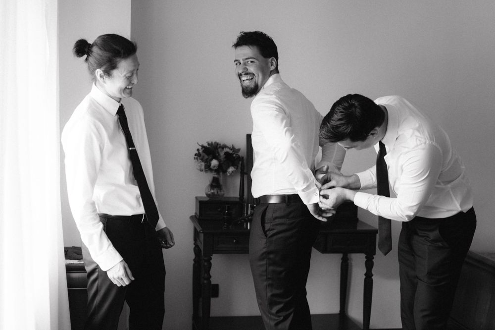 Group of groomsmen in white shirts and ties laughing together while getting ready.