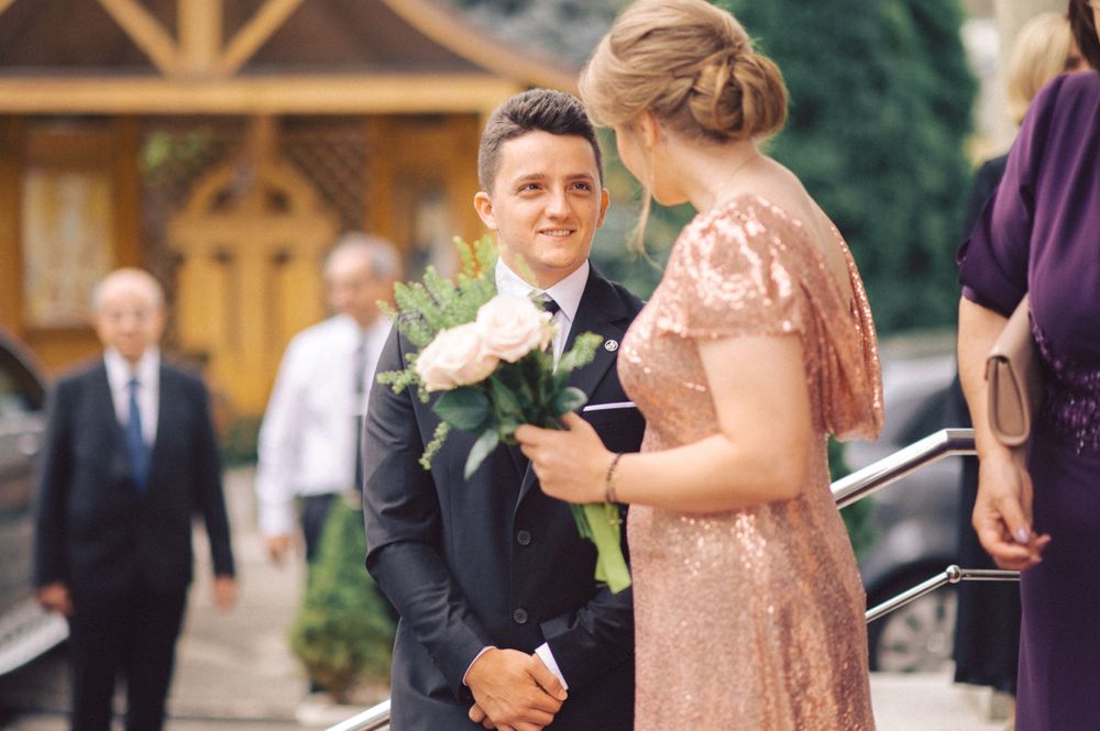 Wedding moment captured outdoors with formal attire and boutonniere exchange.