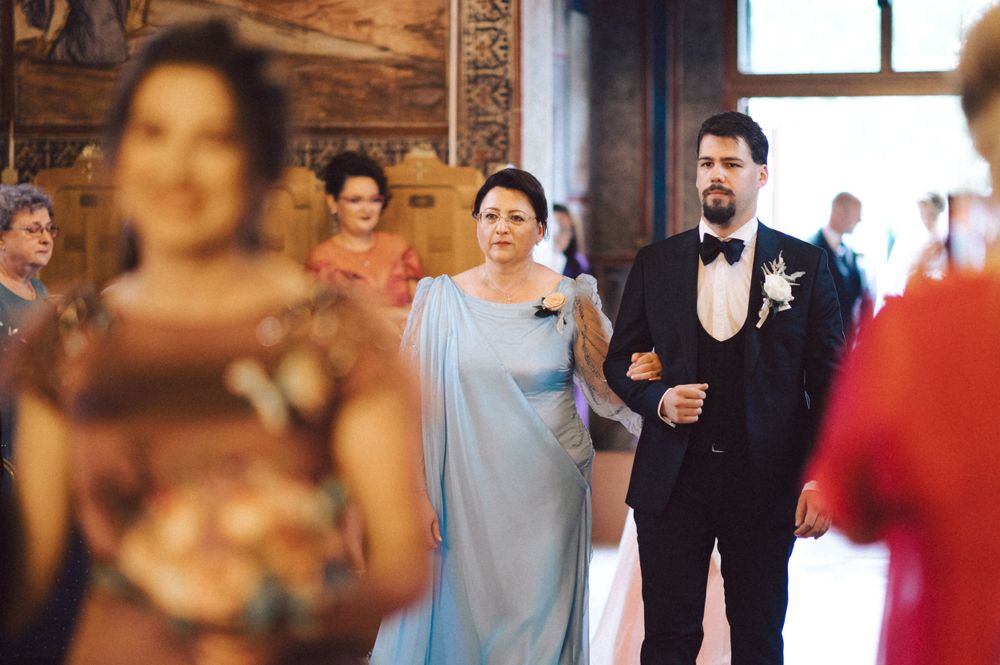 Wedding party walks down aisle in ornate church interior with bridesmaids in light blue dresses.