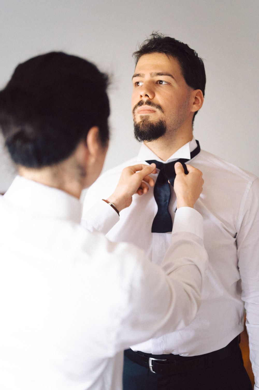 Person helping adjust another person's tie during formal dressing preparation.