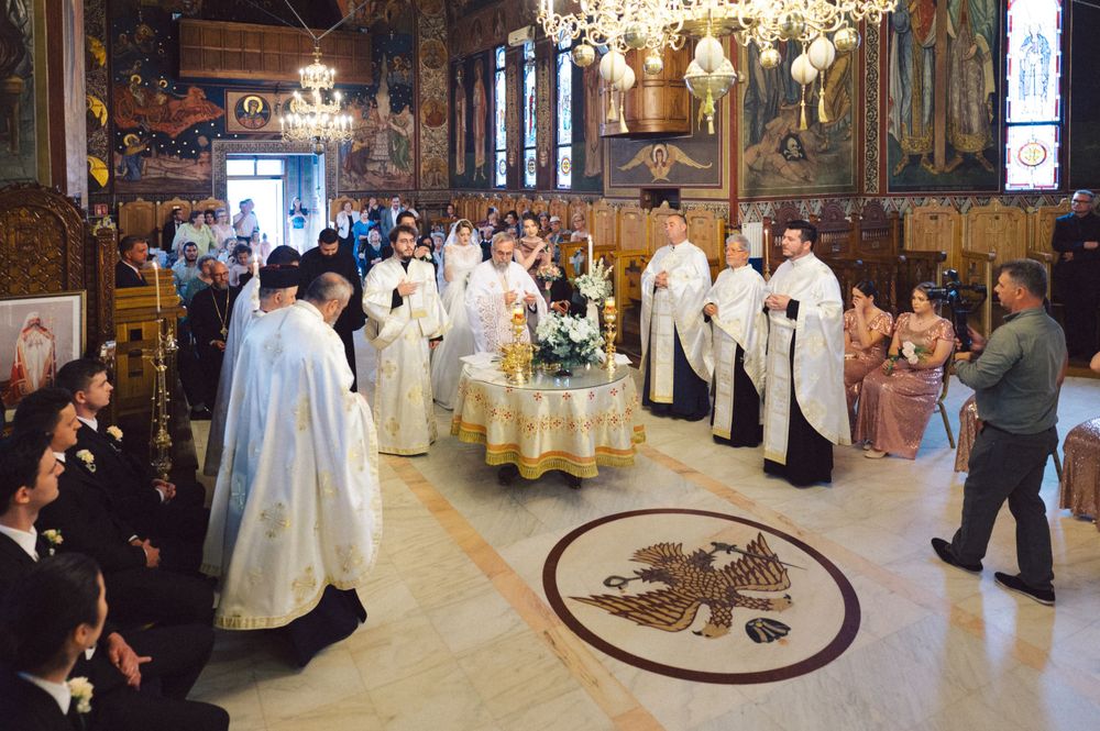 Orthodox church ceremony with clergy in white robes gathered around decorative floor medallion.