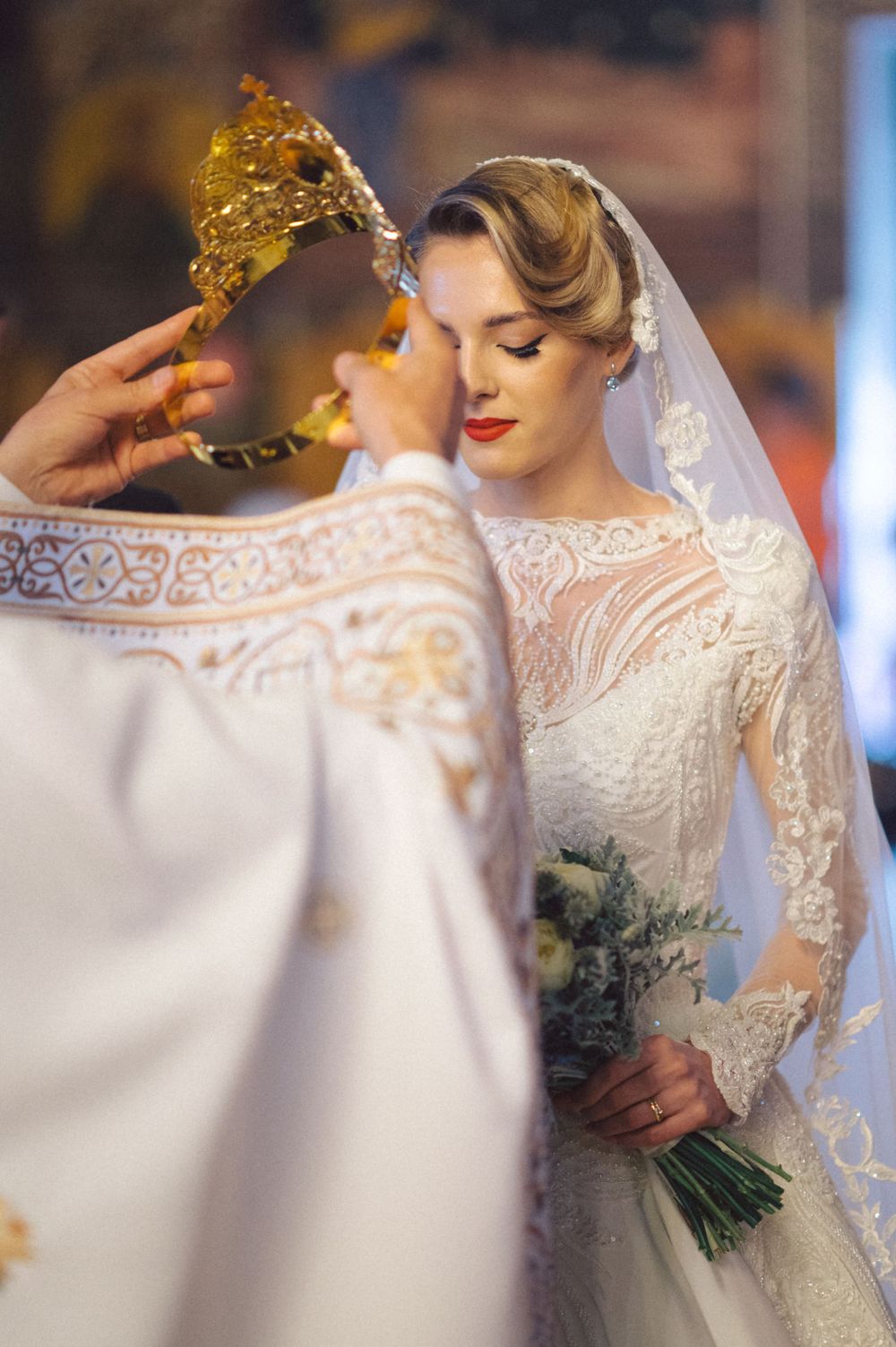 Orthodox wedding ceremony moment with ornate crown blessing and delicate lace dress details.