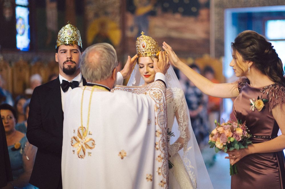 Orthodox wedding ceremony with priest blessing couple wearing traditional ceremonial crowns.