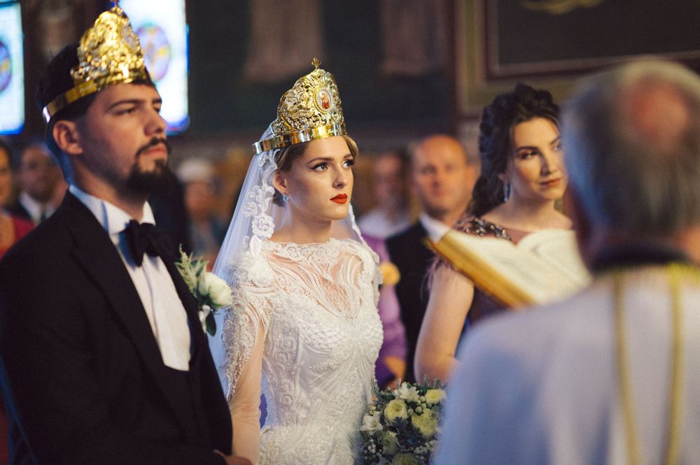Traditional Orthodox wedding ceremony with ornate gold crowns and formal attire in a church setting.