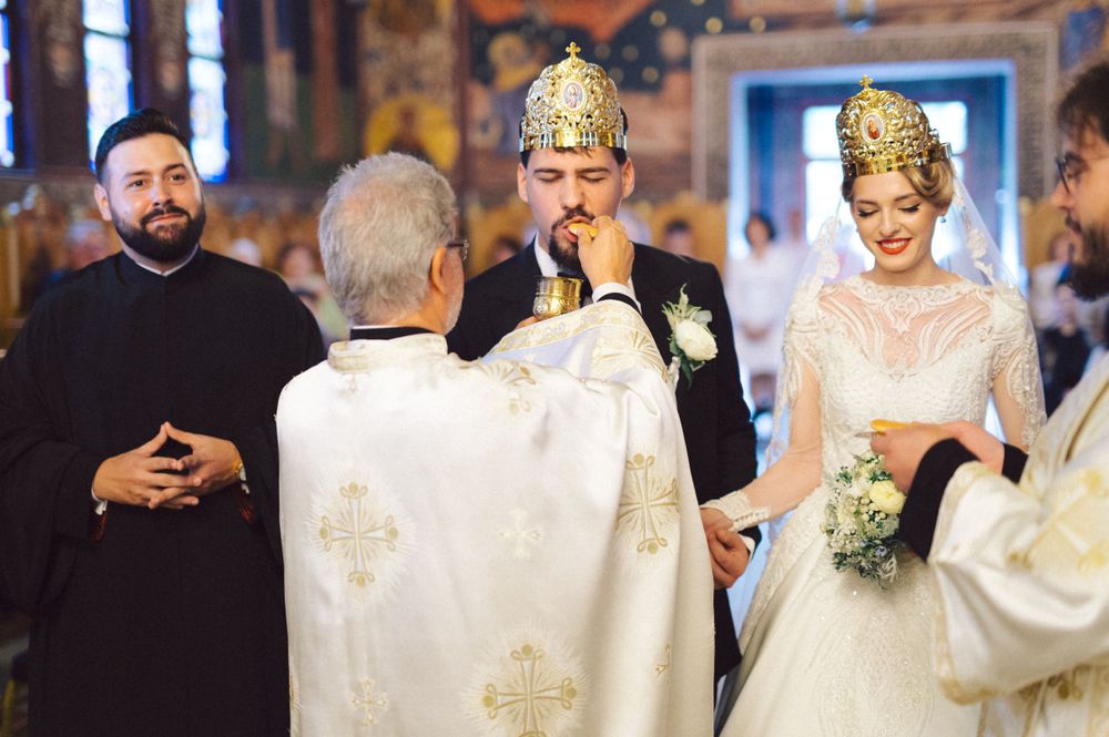 Orthodox wedding ceremony with priests in white robes placing ceremonial crowns during the ritual.