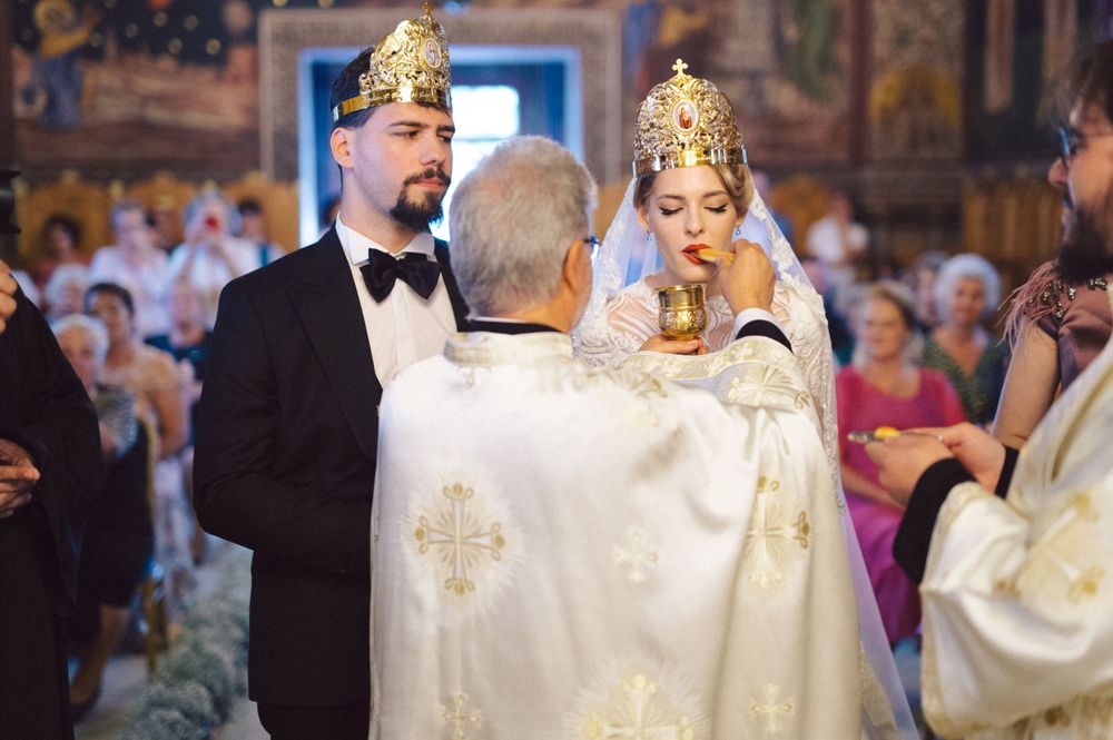 Priest performs Orthodox wedding crowning ceremony in an elaborately decorated church interior.