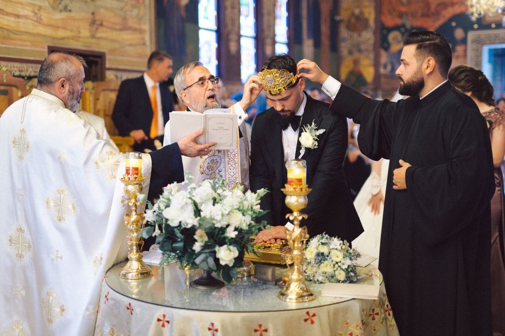 Orthodox wedding ceremony showing priests placing ceremonial crowns with floral arrangements on altar table.