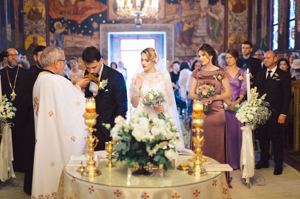Orthodox wedding ceremony in progress with white floral arrangements and golden candlesticks.