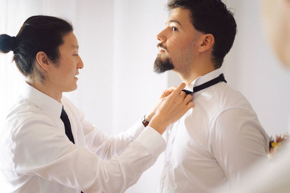 Two people in white dress shirts adjusting formal neckwear.