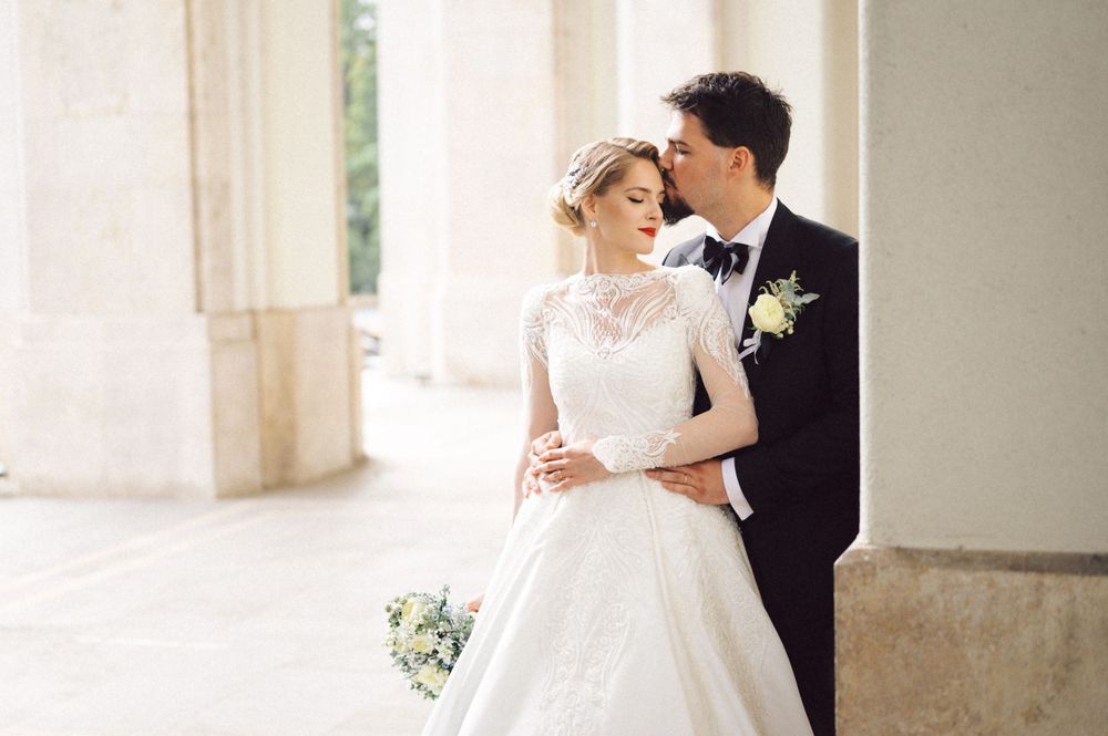 Romantic wedding portrait of couple embracing in elegant colonnade with soft natural light.