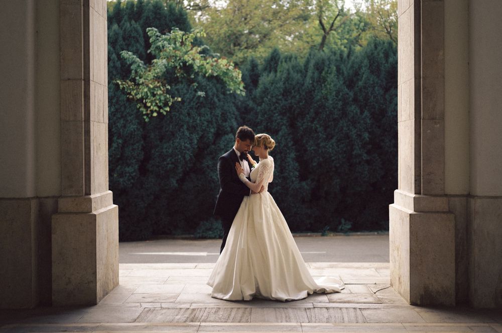 Romantic wedding portrait with couple framed by archway against lush garden background.