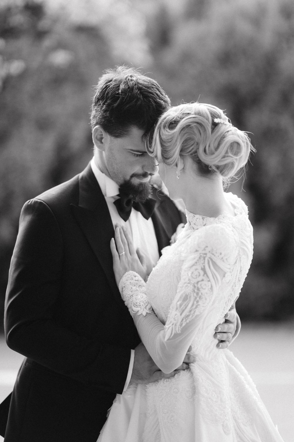 Black and white intimate portrait of wedding couple sharing tender moment outdoors.