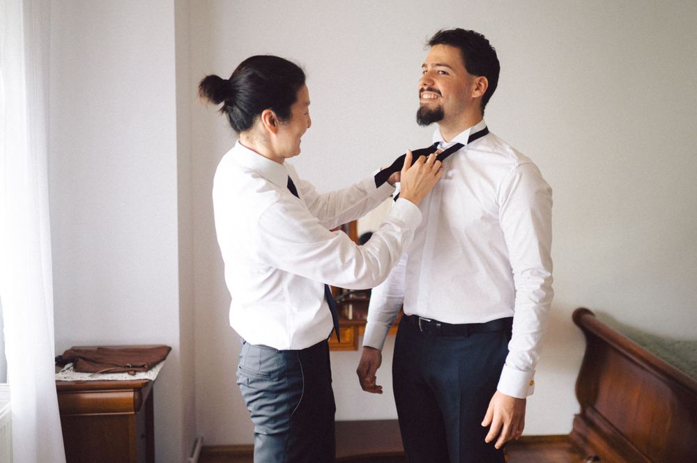 Two people in formal attire assisting with bow tie preparation.