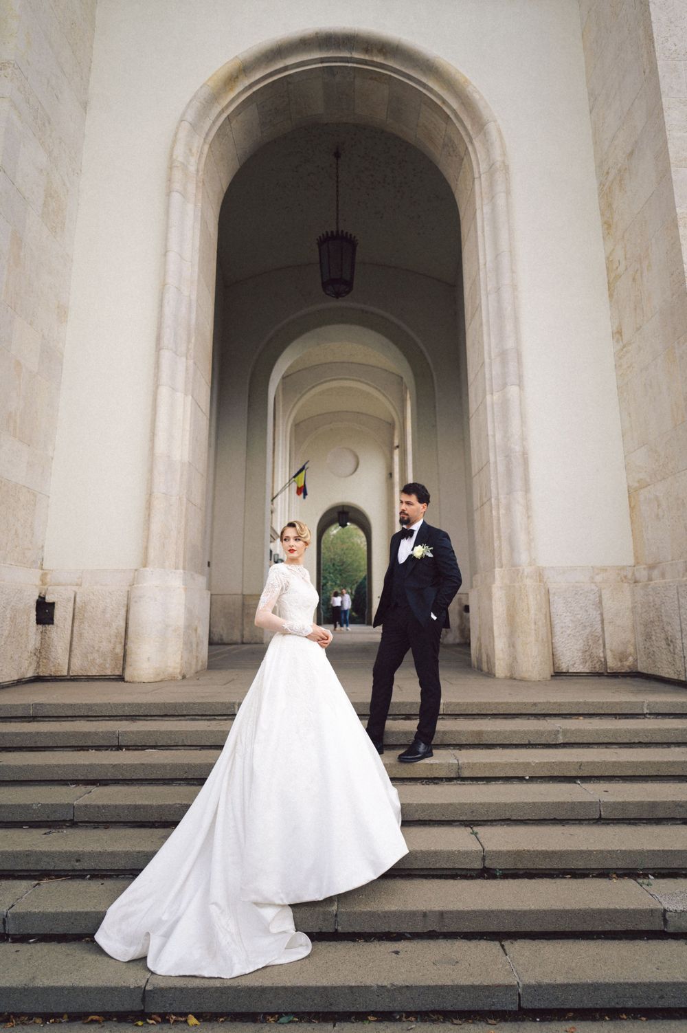 Wedding couple posing on grand stone steps under classic arched entrance of historic building.