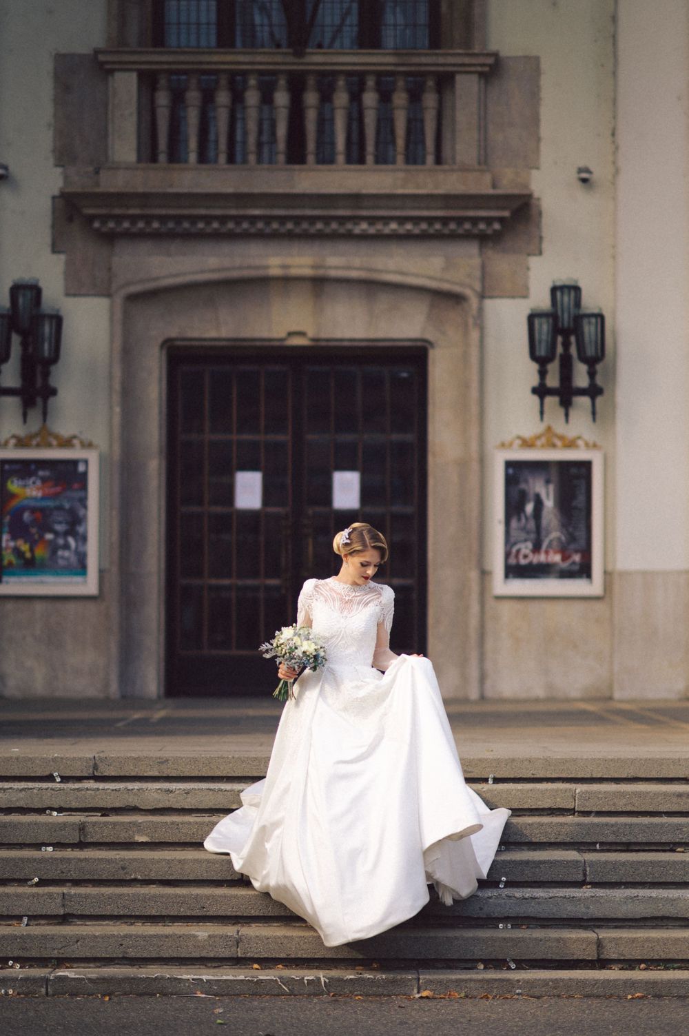 Bride in elegant white ball gown poses solo on stone steps of historic building with ornate architecture.