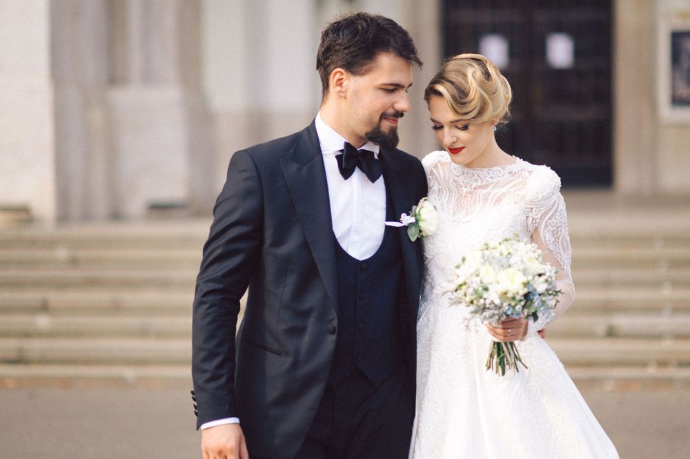 Charming wedding portrait of couple on steps, bride in lace gown holding bouquet of white flowers.