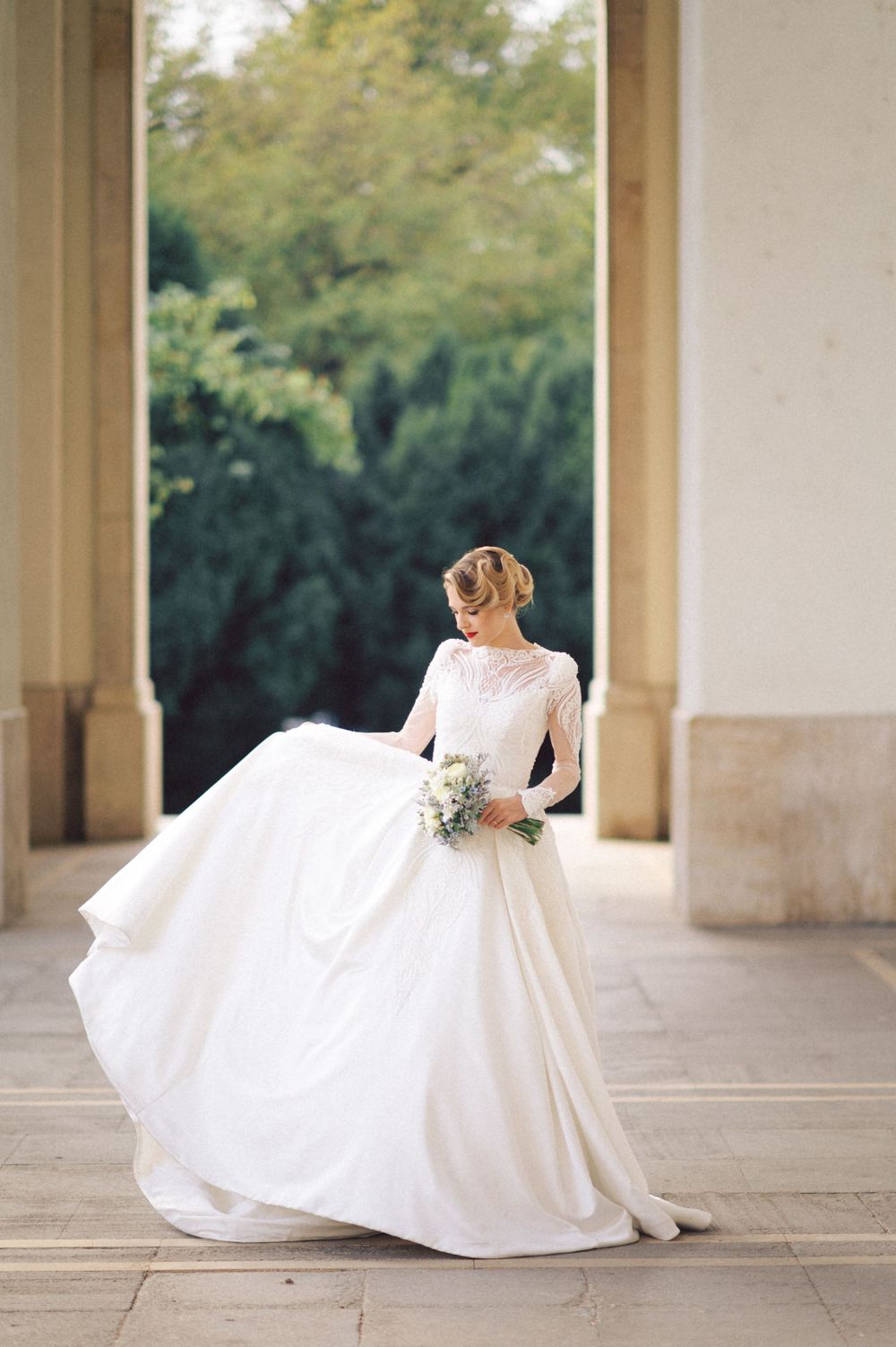 Bride in flowing white wedding dress twirling in outdoor colonnade with flowing skirt movement.