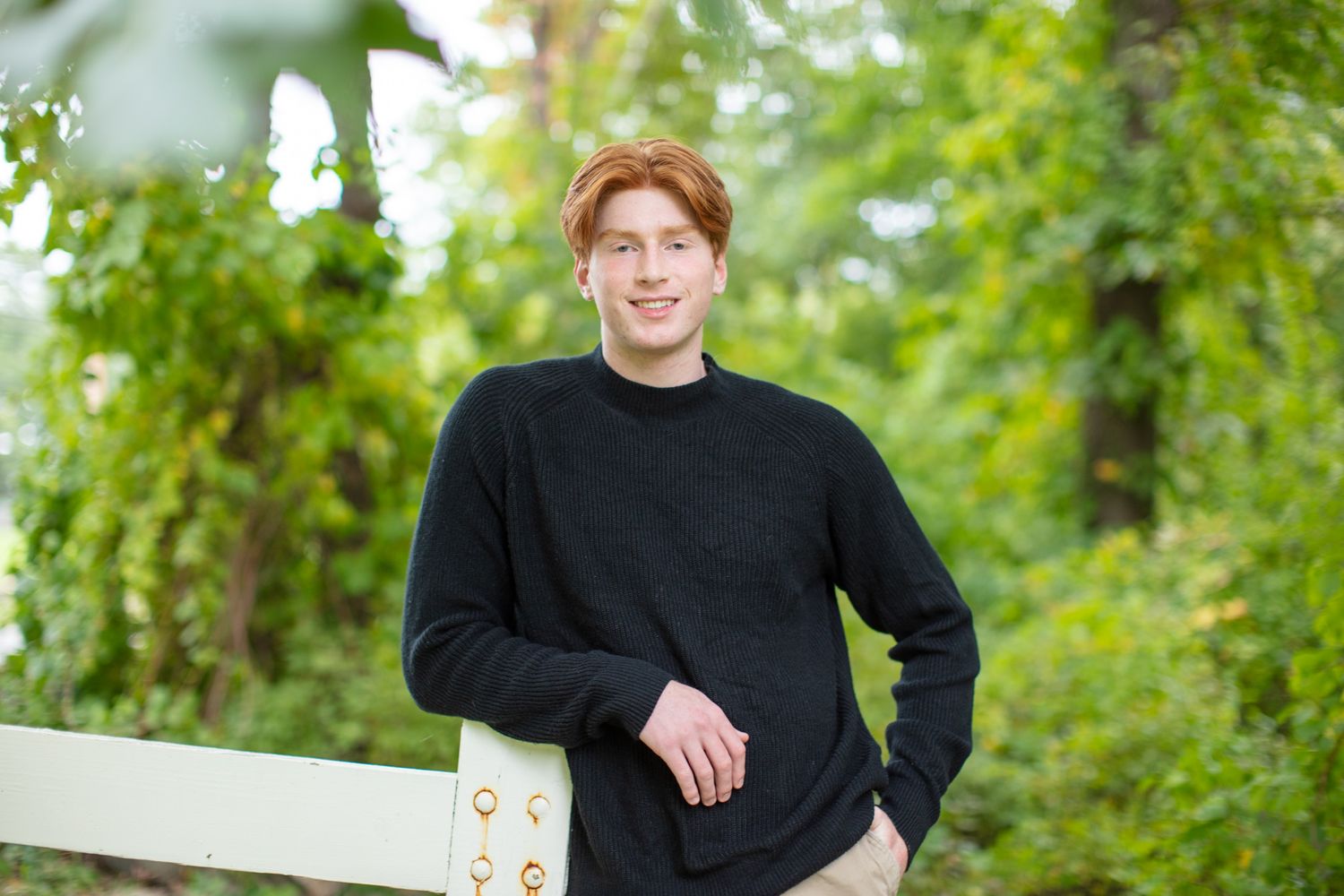 Person in black sweater leans against white fence in lush green garden setting.