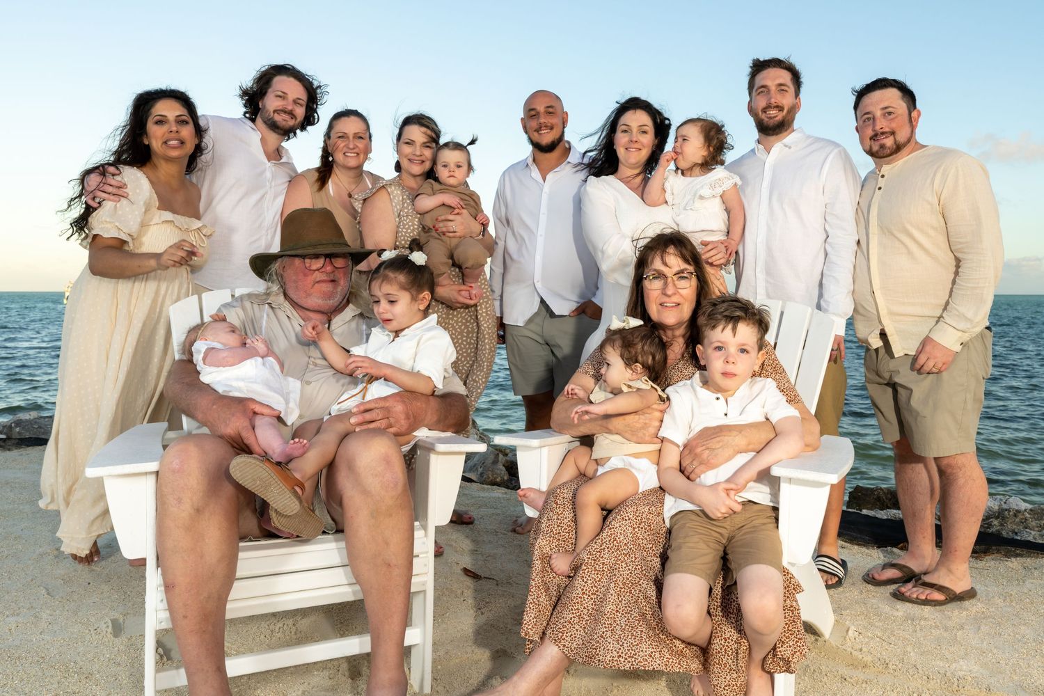 Family beach portrait session with multiple groups wearing coordinated white and beige outfits.