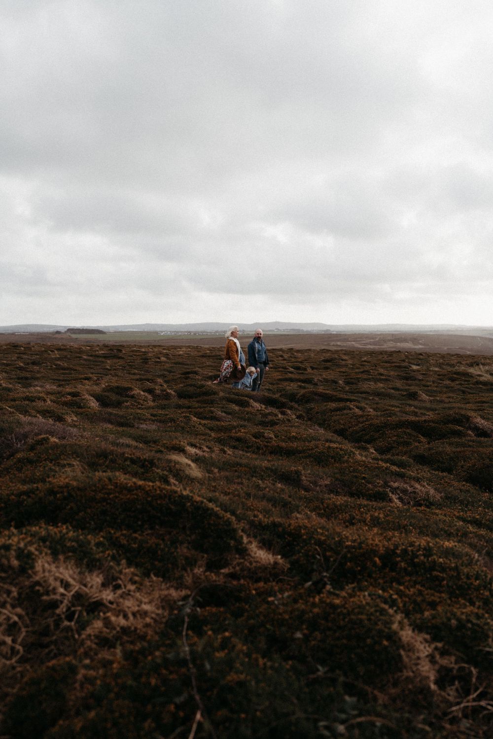 Two figures hiking across a rugged moorland landscape under cloudy skies.