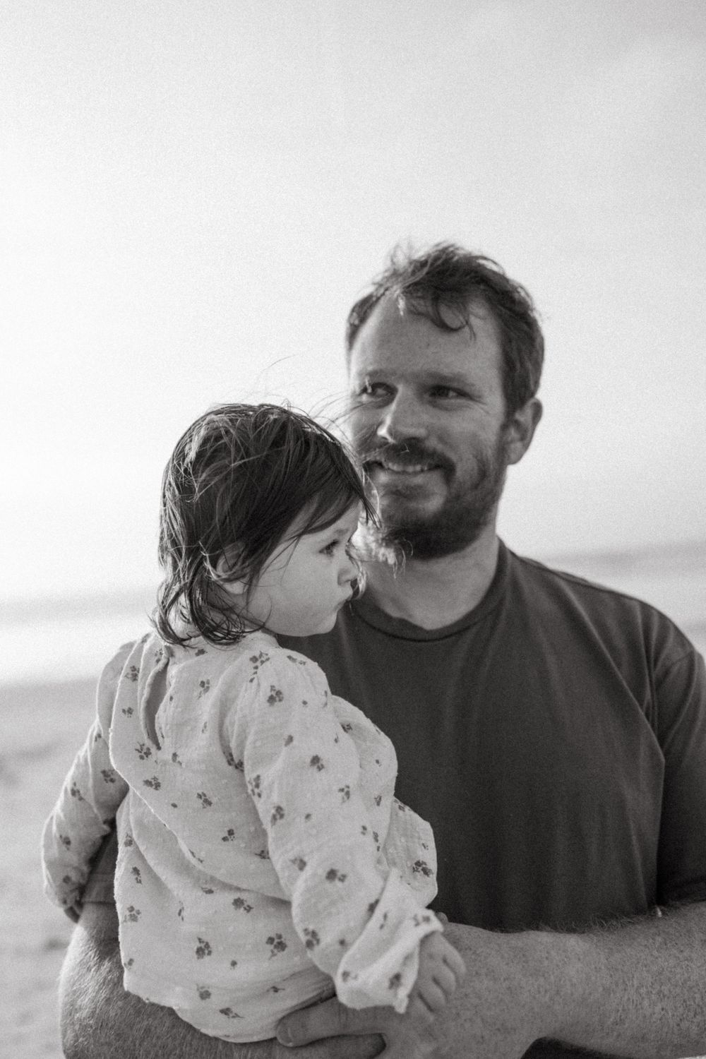 Tender black and white portrait of parent and child at the beach.