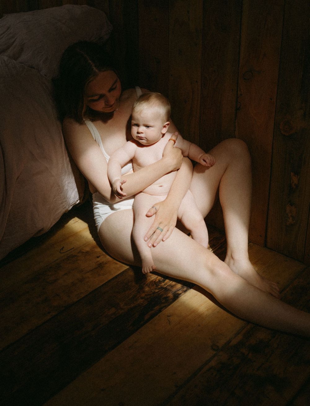 Artistic portrait of parent and baby in dramatic lighting on wooden floor.