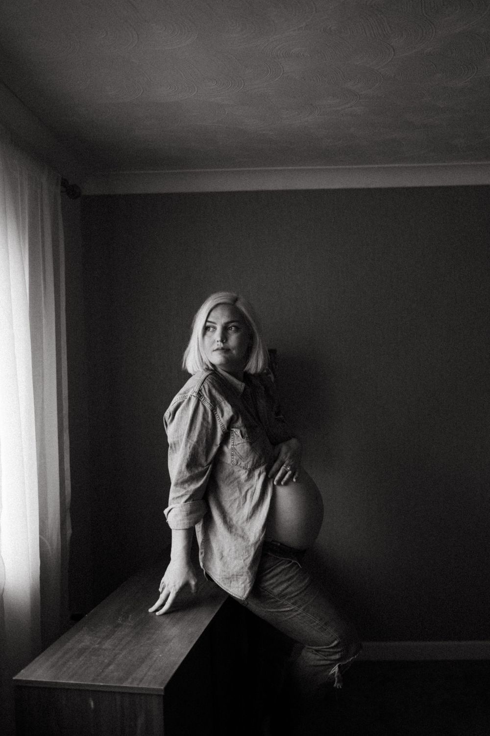 Dramatic black and white maternity portrait near a window.