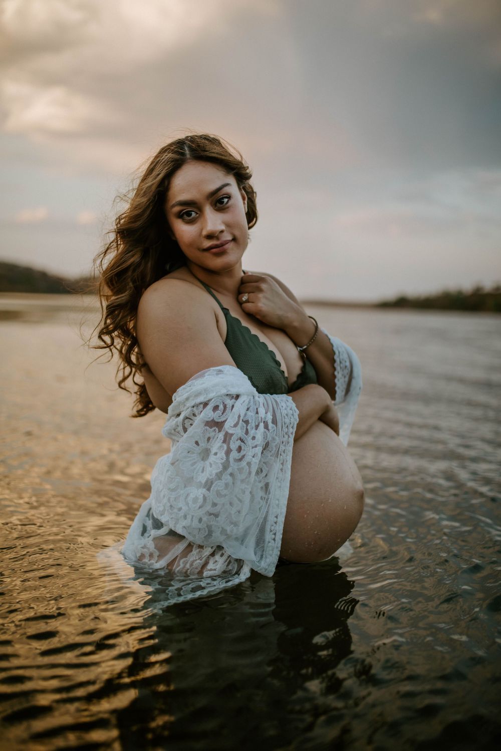 Mama to be embracing belly while standing in water at Lake Moondarra, Mount Isa