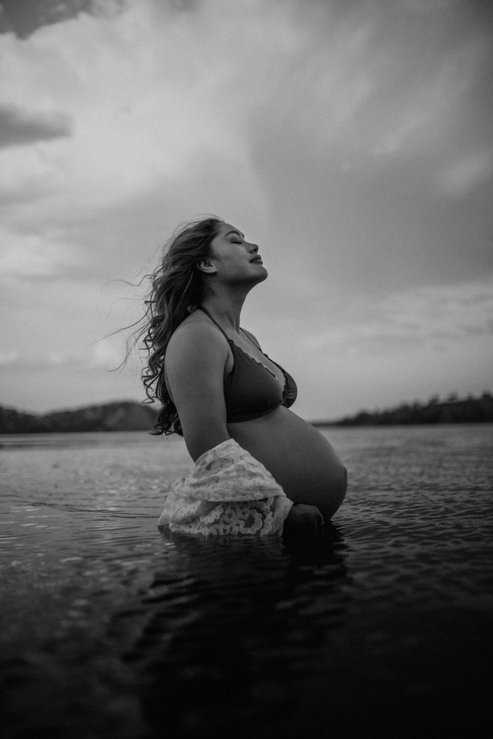 Black and white image of mama to be embracing belly while standing in water at Lake Moondarra, Mount Isa