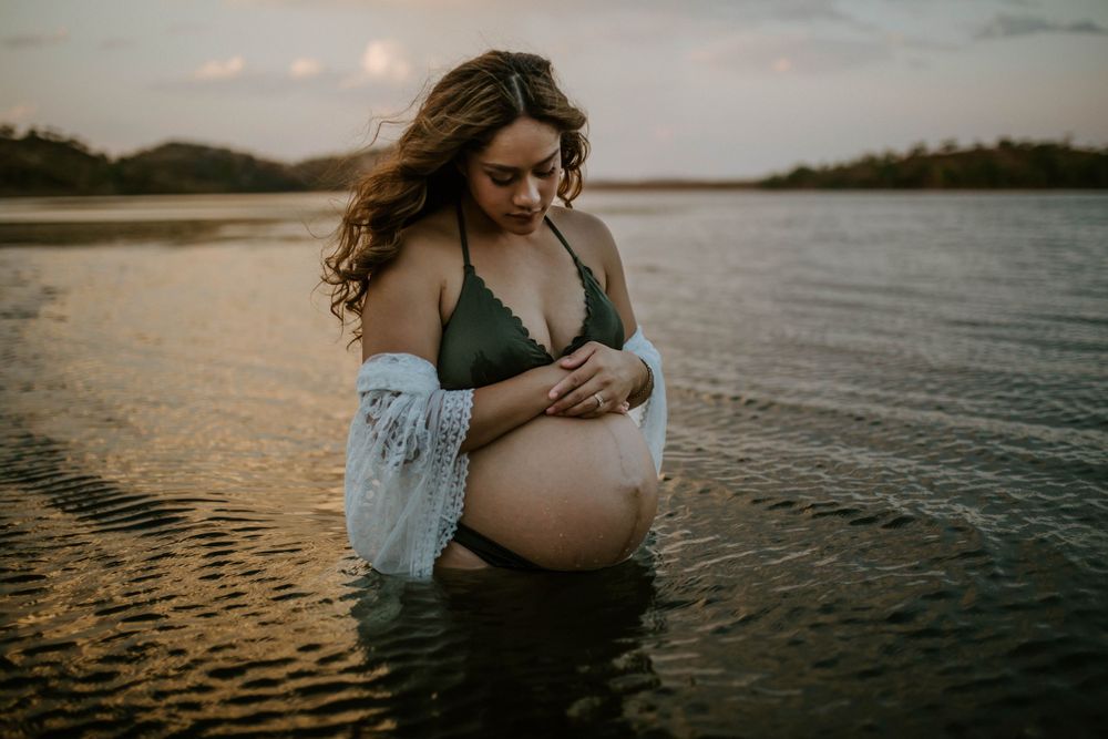 Mama to be embracing belly while standing in water at Lake Moondarra, Mount Isa