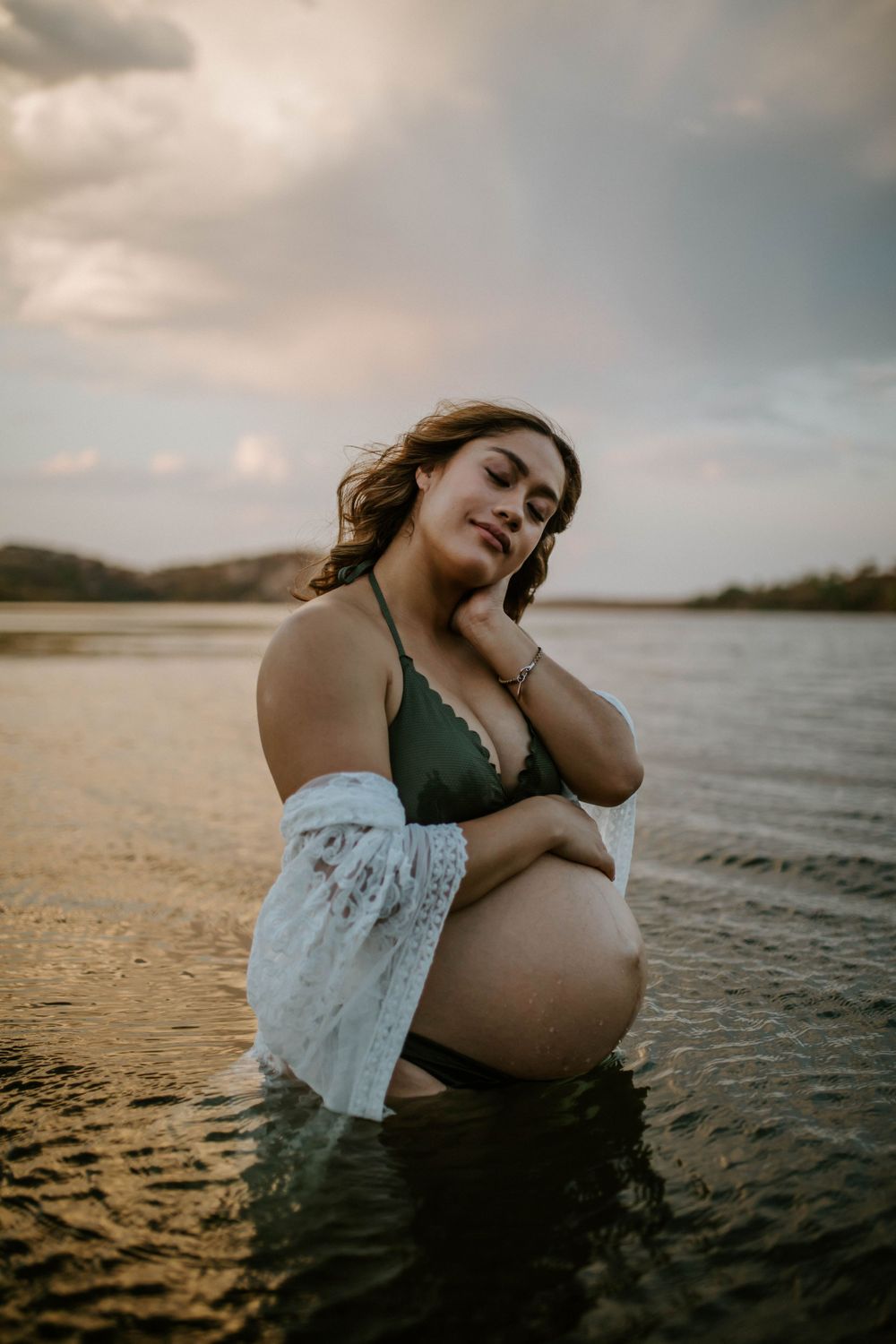Mama to be embracing belly while standing in water at Lake Moondarra, Mount Isa