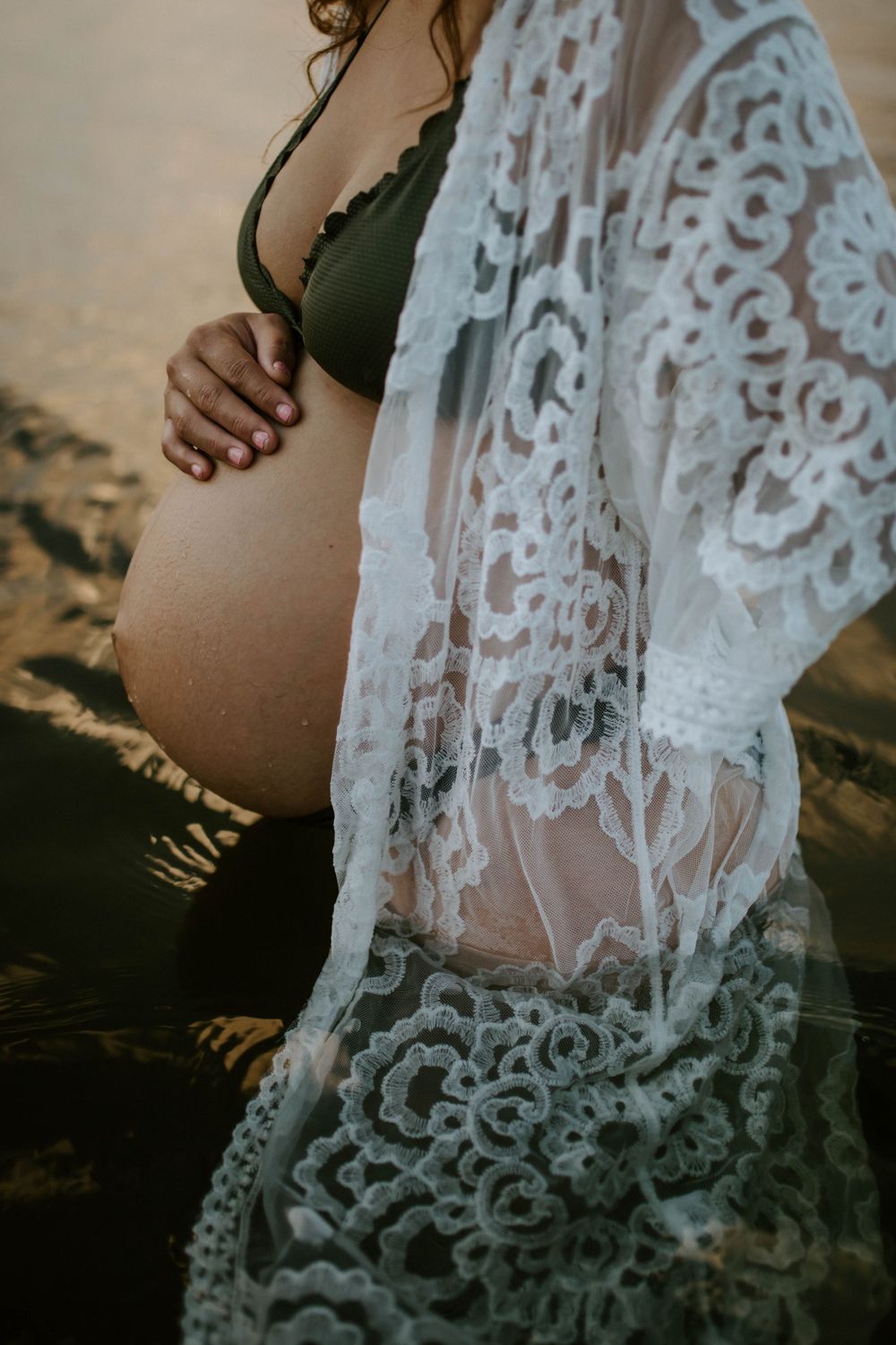 Close up of mama to be embracing belly while standing in water at Lake Moondarra, Mount Isa