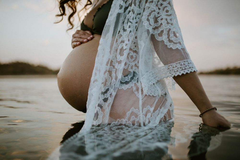 Close up of mama to be embracing belly while standing in water at Lake Moondarra, Mount Isa