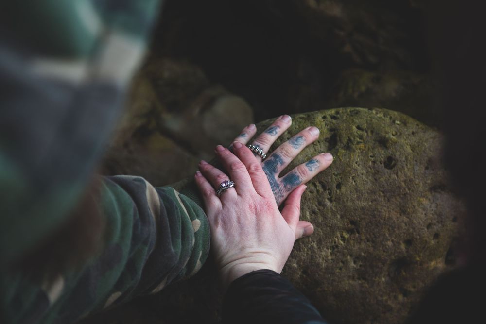 Close-up of two hands touching on mossy rock surface in soft natural light.