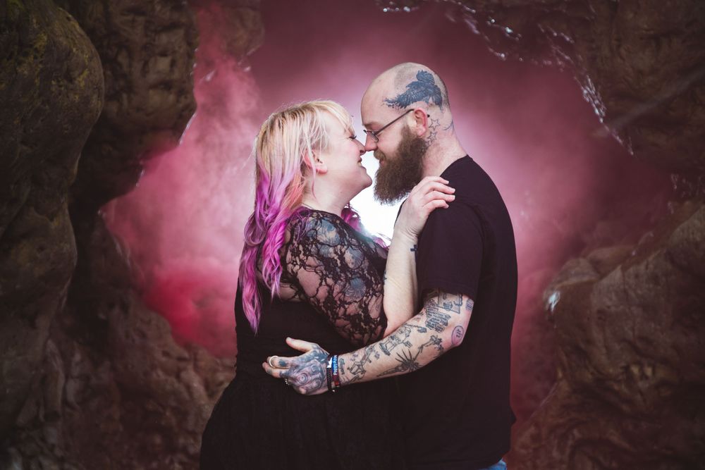 Romantic couple in dramatic pose with pink smoke effect in cave setting.
