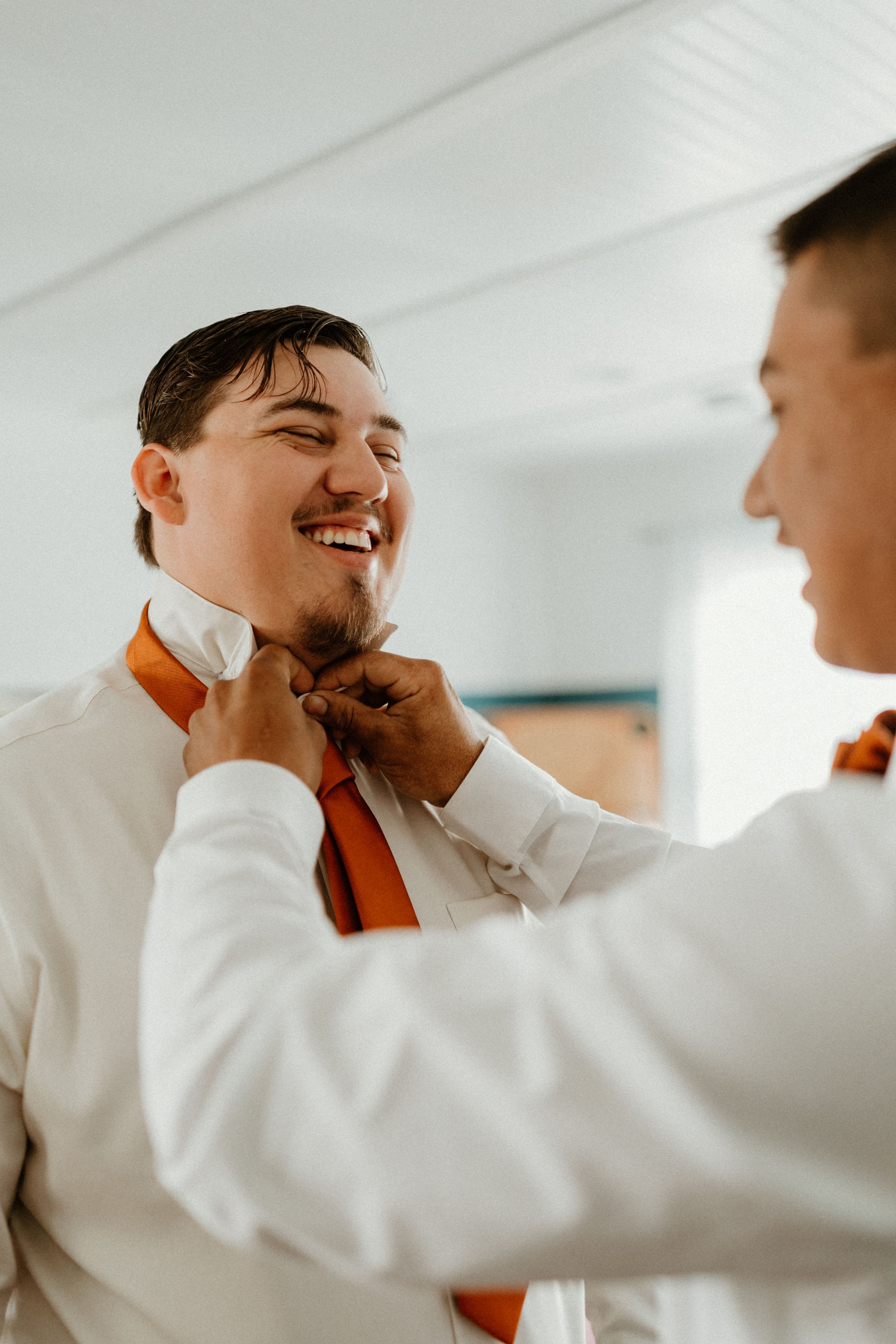 Pre-wedding moment shows someone adjusting an orange tie.