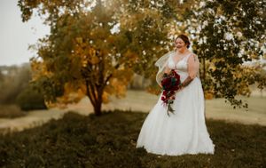 Bride in white wedding dress holding bouquet in autumn outdoor setting.