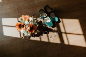 Teal wedding shoes and sunflowers cast shadows on wooden floor.