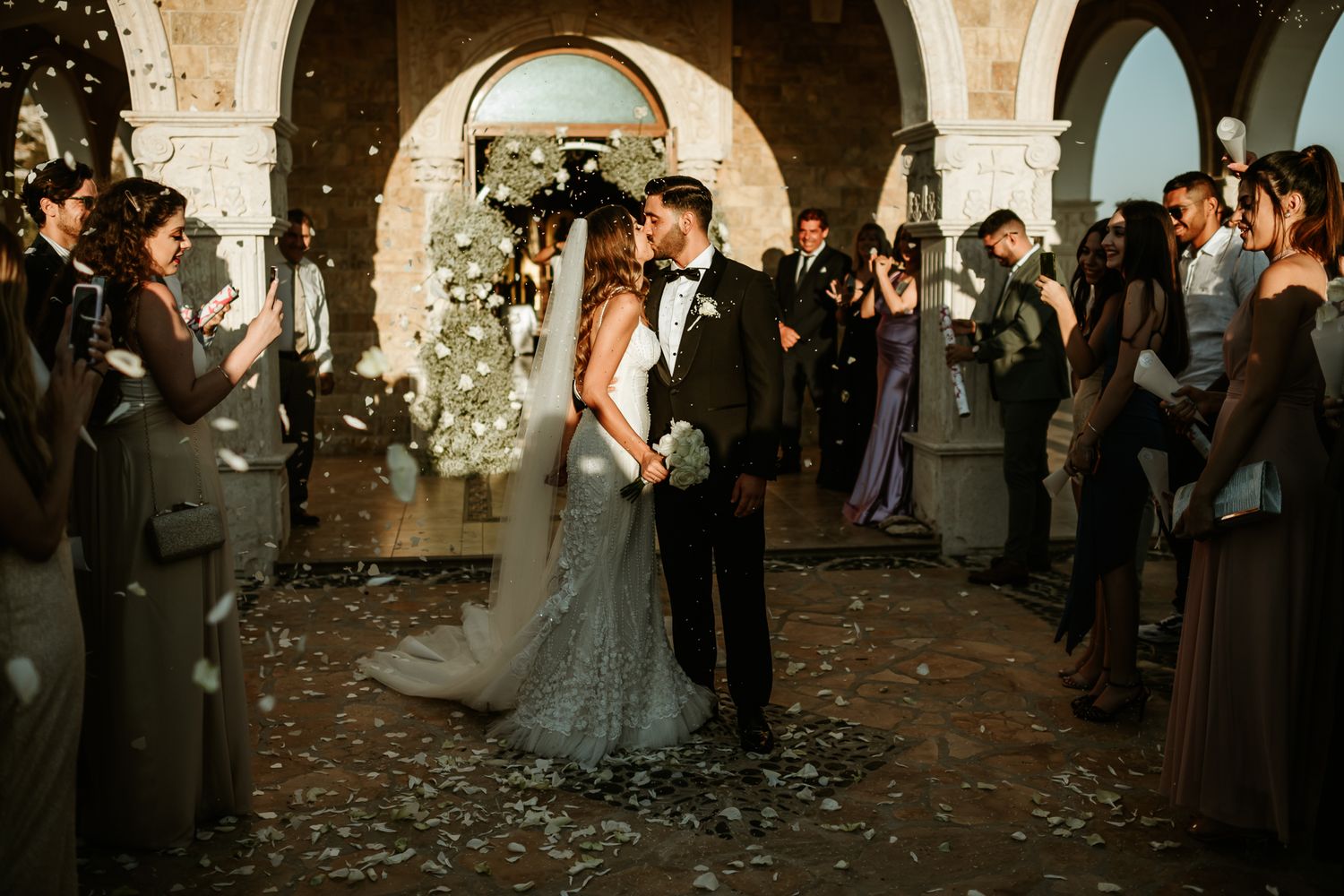 Romantic wedding ceremony taking place under stone arches with confetti falling.