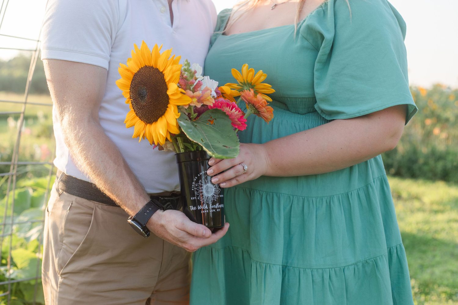 Close-up of hands holding vibrant sunflowers and greenery against a sunny outdoor background.