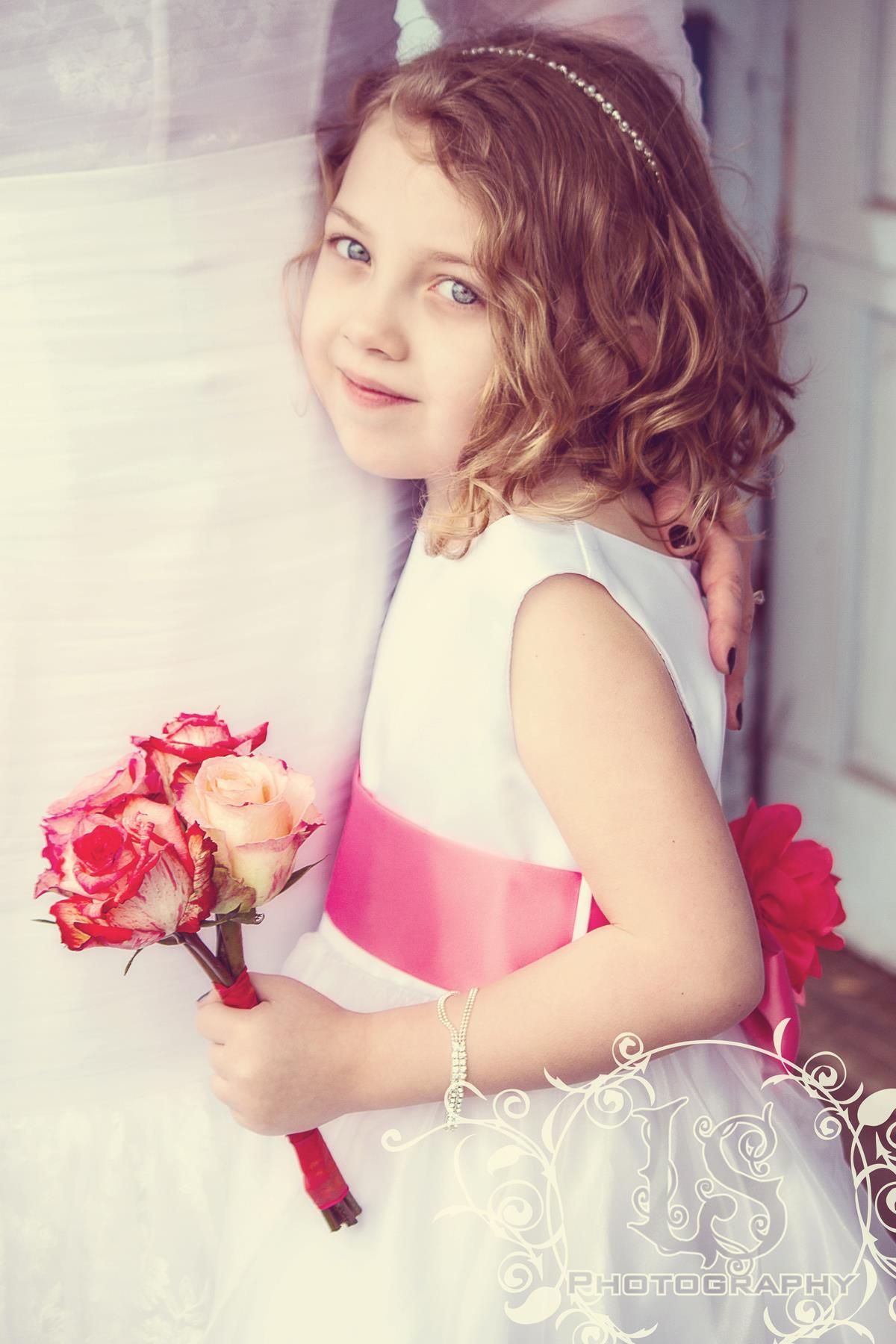 Young flower girl in pink dress holding roses in dreamy portrait series.