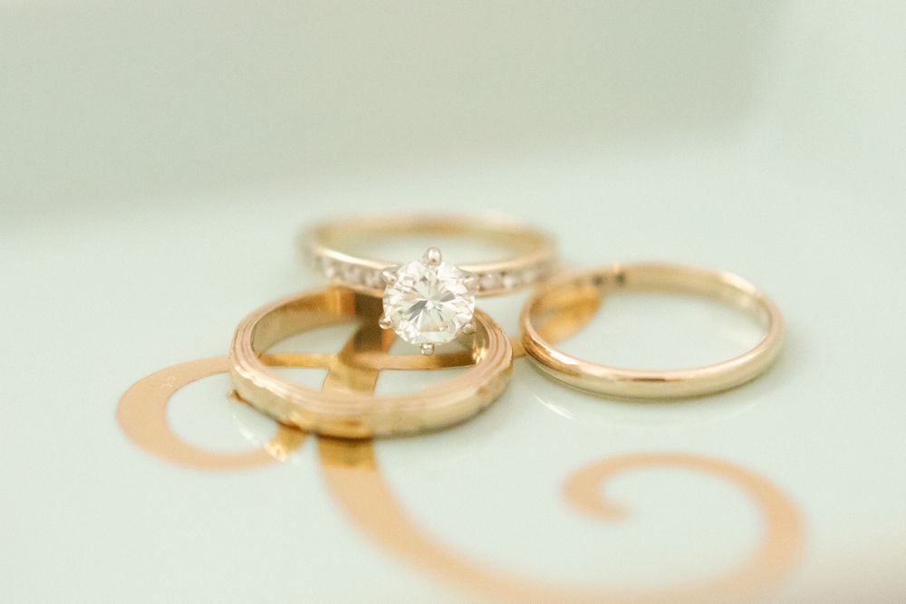 Three gold wedding rings including a diamond solitaire engagement ring stacked on a monogram ring dish.